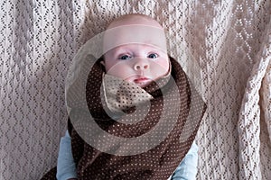 Cute baby with big blue eyes wearing a hat and a huge knitted scarf