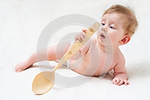 Cute baby with a big wooden spoon. Little cook on a light background