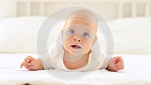 a cute baby with blue eyes of six months is lying on a bed in a white bodysuit in a bright bedroom, a beautiful newborn