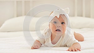 a cute baby with blue eyes of six months is lying on a bed in a white bodysuit in a bright bedroom, a beautiful newborn