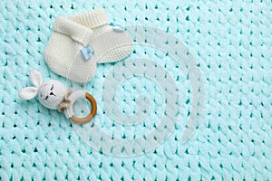 Cute baby booties and toy on light blue knitted fabric, flat lay. Space for text