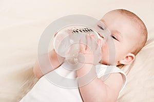 Cute baby with a bottle of milk on a beige blanket