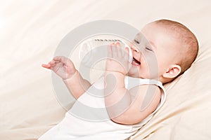 Cute baby with a bottle of milk on a beige blanket