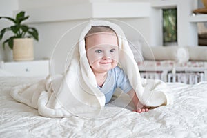 Cute baby boy 6 months old in blu bodysuit smiling and lying on bed with white plaid at home