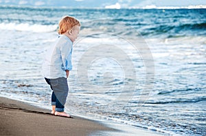 Cute baby boy on the beach, admiring the sea. Bare feet. Happy