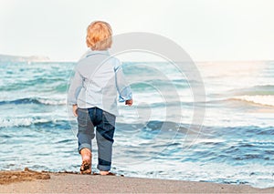 Cute baby boy on the beach, admiring the sea. Bare feet. Happy