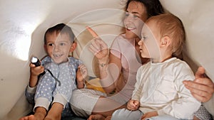 Cute baby boy with brother and mother playing with flashlight and shadows under blanket in bed. Family having time together,