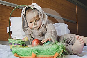 Cute baby boy in the bunny costume playing with the basket with colorful easter eggs. Easter egg hunt and baby development