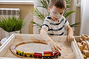 Cute baby boy confident playing railroad train toy on sand table therapy childish early development