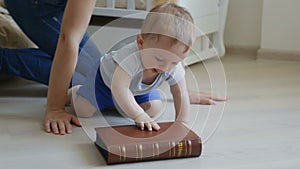 Cute baby boy crawling on floor and trying to open big book