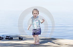 Cute baby boy is crying on the beach with a beautiful blue sea in the background. Portrait of an alone sad child on a beach