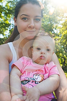 Cute baby boy with Down syndrome and his young mother in summer day