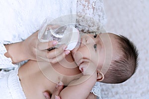 Cute baby boy drinking water from bottle with his mom. Hand of asian young woman holding bottle with water while feeding