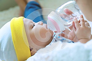 Cute baby boy drinking water from bottle with his mom. Hand of asian young woman holding bottle with water while feeding