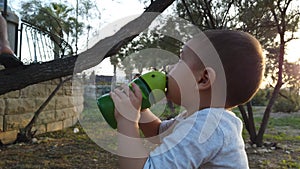 Cute baby boy drinking water in the park during sunset