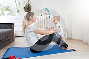 Cute baby boy exercising with young mother on fitness mat at home