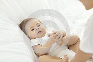 Cute baby boy or girl is lying in an infant bed and looking at his or her mother