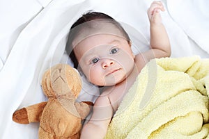 The cute baby boy is happy with yellow blanket and doll bear lovely friend on the white bed