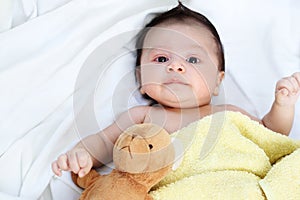The cute baby boy is happy with yellow blanket and doll bear lovely friend on the white bed
