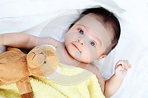 The cute baby boy is happy with yellow blanket and doll bear lovely friend on the white bed