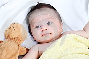 The cute baby boy is happy with yellow blanket and doll bear lovely friend on the white bed