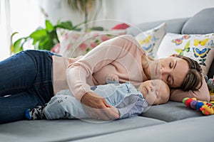 Cute baby boy and his mother, lying on the couch in living room