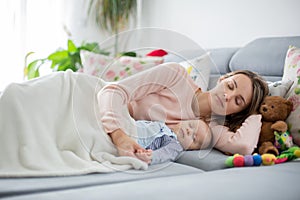 Cute baby boy and his mother, lying on the couch in living room