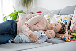 Cute baby boy and his mother, lying on the couch in living room