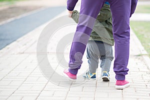 Cute baby boy learning to walk and make his first steps. mom is holding his hand. child`s feet close up, view from the