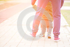 Cute baby boy learning to walk and make his first steps. mom is holding his hand. child`s feet close up, view from the