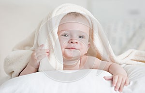 Cute baby boy lying under white blanket on bed