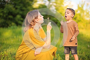 Cute baby boy and mother blowing on a dandelions on green lawn. Summertime photography for ad or blog about motherhood