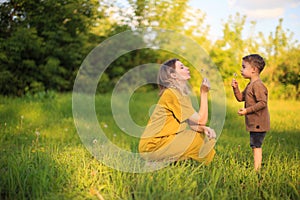 Cute baby boy and mother blowing on a dandelions on green lawn. Summertime photography for ad or blog about motherhood