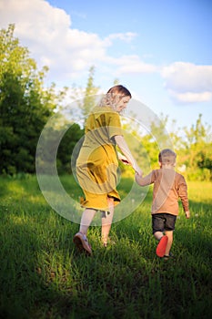 Cute baby boy and mother walking on green lawn. Back view. Summertime photography for ad or blog about motherhood photo