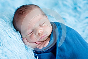 Cute baby boy, peacefully sleeping wrapped in blue wrap