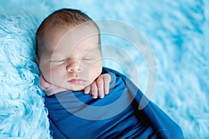 Cute baby boy, peacefully sleeping wrapped in blue wrap