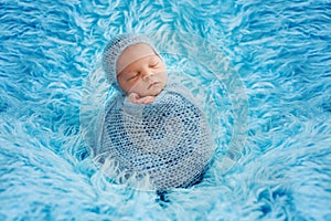 Cute baby boy, peacefully sleeping wrapped in blue wrap on a blu