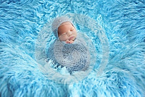 Cute baby boy, peacefully sleeping wrapped in brue wrap on a blu