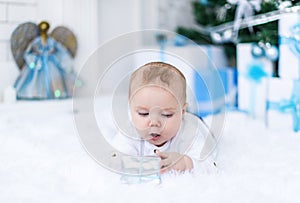 Cute baby boy playing with christmas gift in white room.