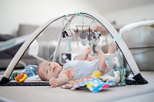 Cute baby boy playing with hanging toys arch on mat at home Baby activity and play center for early infant development