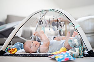 Cute baby boy playing with hanging toys arch on mat at home Baby activity and play center for early infant development