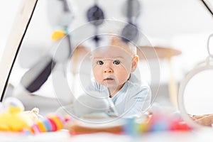 Cute baby boy playing with hanging toys arch on mat at home Baby activity and play center for early infant development