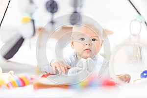 Cute baby boy playing with hanging toys arch on mat at home Baby activity and play center for early infant development