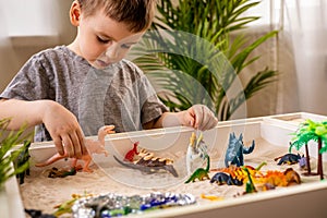 Cute baby boy playing sensory box kinetic sand table with carnivorous and herbivorous dinosaurs