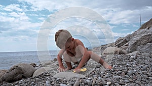 Cute baby boy playing with a shovel and stones on the beach, on the seashore. Summer holidays and sea holidays.