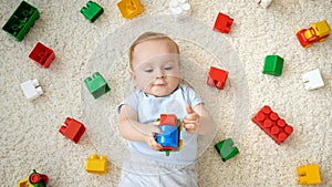 Cute baby boy playing toy car on carpet next to heap of colroful toys, blocks and bricks. Concept of children