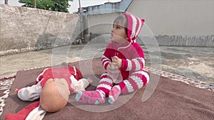 Cute baby boy in red woolen winter clothing with bottle looking wonder. Kid sitting on carpet on the roof at home in sunlight.