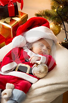 Cute baby boy in Santa costume sleeping ext to Christmas gifts