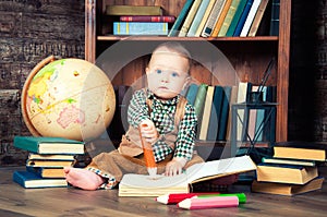 Cute baby boy sitting with globe, books and drawing pencils