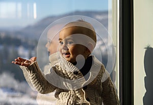 Cute baby boy sitting beside a window wearing warm sweater